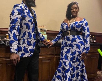 May include: A couple wearing matching blue and white patterned outfits. The man is wearing a blazer and black pants, and the woman is wearing a long-sleeved dress. Both are wearing gold crowns and sunglasses.