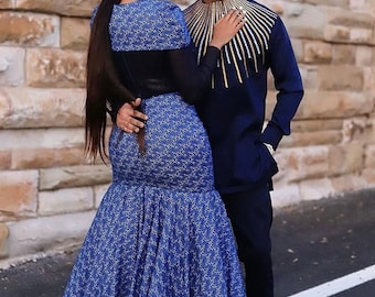 Puede incluir: Una pareja vestida con atuendos azules a juego. La mujer lleva un vestido azul y blanco con un turbante azul. El hombre lleva una camisa azul con adornos dorados y blancos. Están de pie frente a una pared de ladrillo.