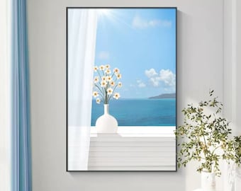 May include: A rectangular wall art print featuring a white vase filled with white flowers sitting on a ledge. The background shows a bright blue sky with clouds, a sun flare, and a calm ocean view. A sheer white curtain hangs on the left side.