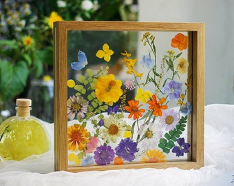 May include: A wooden frame with a pressed flower display. The flowers are arranged in a random pattern and include yellow, orange, purple, blue, and white flowers.