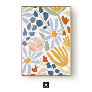 May include: Floral art print in a gold frame. The artwork features a colorful, abstract floral design with daisies, leaves, and other stylized flowers in shades of blue, orange, yellow, and pink on a white background. The letter "A" is in the bottom corner.