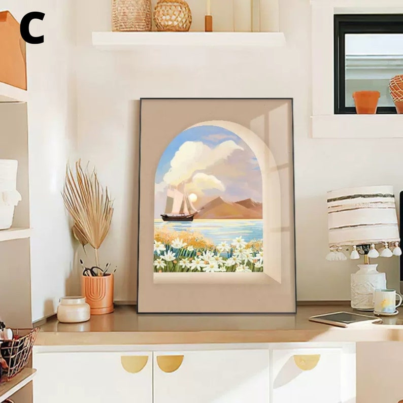 May include: A framed print of a seascape with a sailboat in the distance, framed by an archway with white flowers in the foreground. The print is in a black frame with a beige mat.