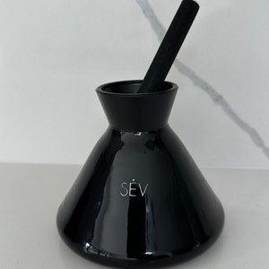 May include: A black ceramic diffuser with a black wooden stick. The diffuser has the word "SEV" printed on the front.