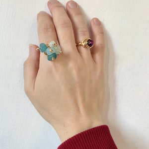 Puede incluir: Dos anillos de oro con piedras preciosas. El primer anillo tiene un grupo de piedras preciosas azul claro y turquesa. El segundo anillo tiene una sola piedra preciosa redonda, de color morado oscuro.