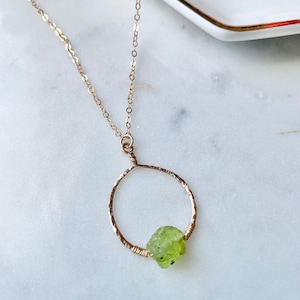 Puede incluir: Un collar de oro con un colgante circular martillado y una piedra de peridoto verde.