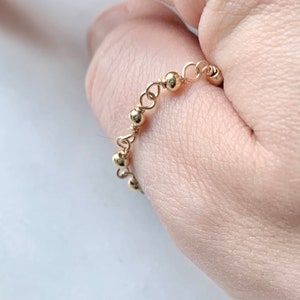 May include: A gold beaded ring with a delicate chain design. The ring is worn on a finger.