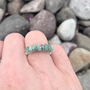 Könnte beinhalten: Ein Silberdrahtring mit einer Reihe von hellgrünen Edelsteinen. Der Ring befindet sich an einem Finger.