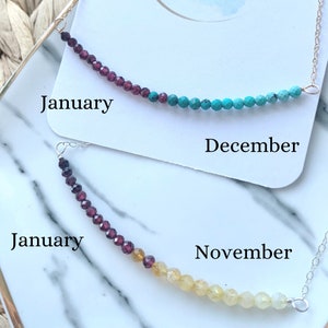 Peut inclure: Deux colliers avec des perles de pierres de naissance. Le collier du haut a des perles rouges et turquoise et dit "Janvier" et "Décembre". Le collier du bas a des perles rouges et jaunes et dit "Janvier" et "Novembre".
