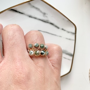 Könnte beinhalten: Ein goldfarbener, drahtgewickelter Ring mit grünen und weißen Achatperlen. Der Ring befindet sich an einer Hand, die einen ähnlichen Ring trägt.