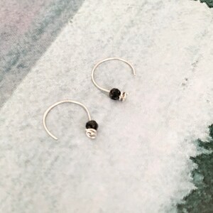 May include: A pair of silver hoop earrings with small black beads attached to the hoops.