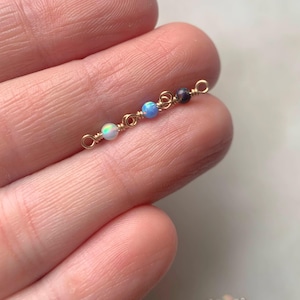May include: A close-up of a gold chain with four small opal beads. The beads are in shades of blue, white, and black.