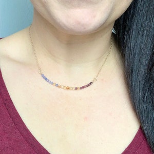 May include: A gold chain necklace with a graduated row of gemstone beads in shades of blue, orange, and purple.