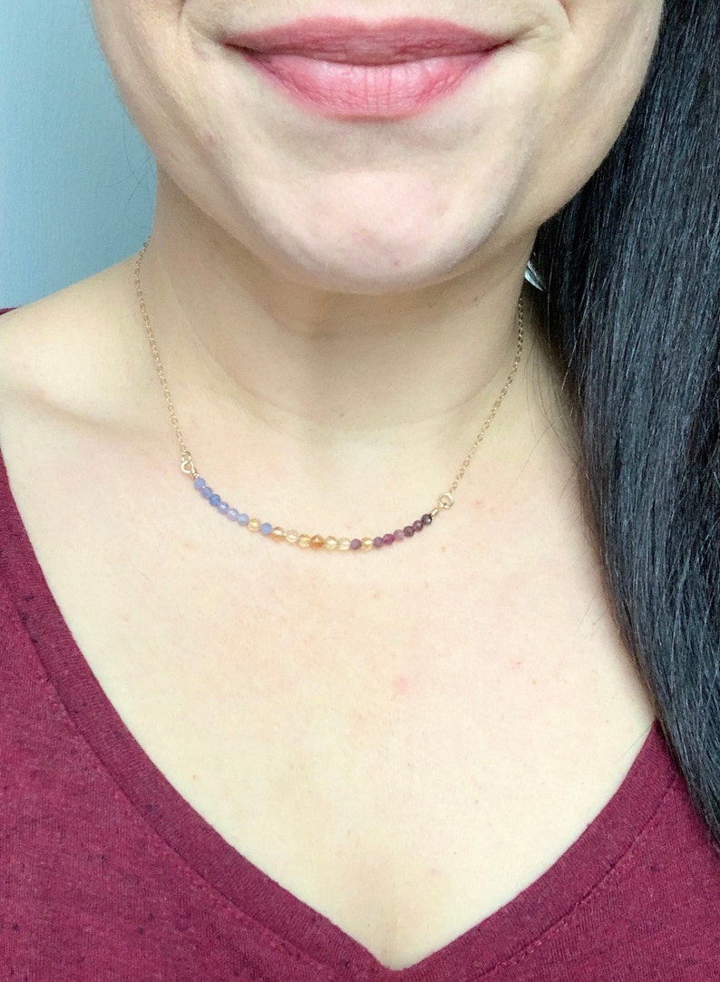 May include: A gold chain necklace with a graduated row of gemstone beads in shades of blue, orange, and purple.