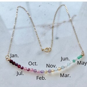 May include: A gold chain necklace with a row of colorful gemstone beads representing each month of the year. The beads are arranged in a gradient from dark red to light green. The months are labeled on the image: Jan., Jul., Oct., Nov., Feb., Mar., Jun., and May.