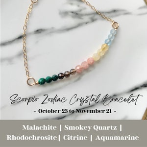 May include: A gold chain bracelet with a row of colourful gemstones, including malachite, smoky quartz, rhodochrosite, citrine, and aquamarine. The bracelet is labelled "Scorpio Zodiac Crystal Bracelet - October 23 to November 21 -"