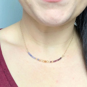 Op de afbeelding: Een gouden ketting met een aflopende ombre van lichtblauw, geel en paarse kralen.