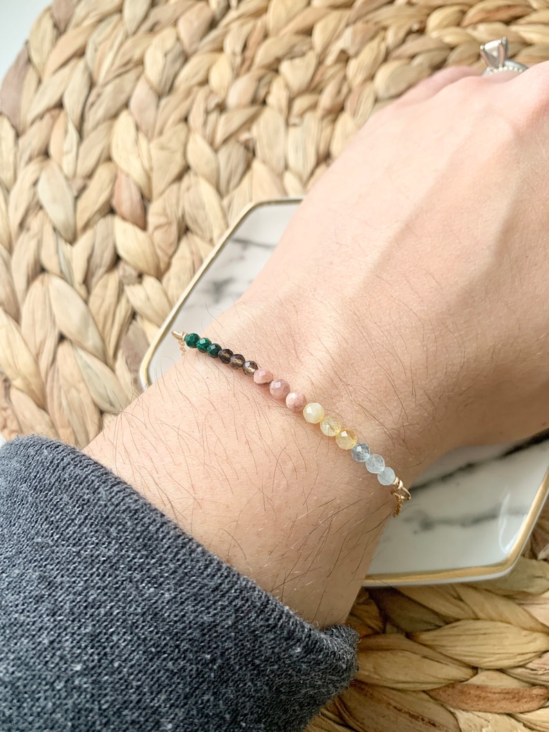 May include: A gold chain bracelet with green, brown, pink, yellow, and blue gemstone beads.
