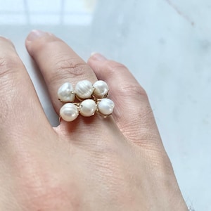 Könnte beinhalten: Ein Ring aus Golddraht mit einem Cluster aus weißen Perlen. Der Ring wird an einem Finger getragen.