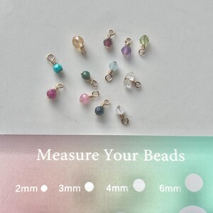 May include: A collection of colorful gemstone beads with gold-colored findings. The beads vary in color, including teal, pink, green, and purple. The image also includes a guide to measure the beads, with sizes ranging from 2mm to 12mm.