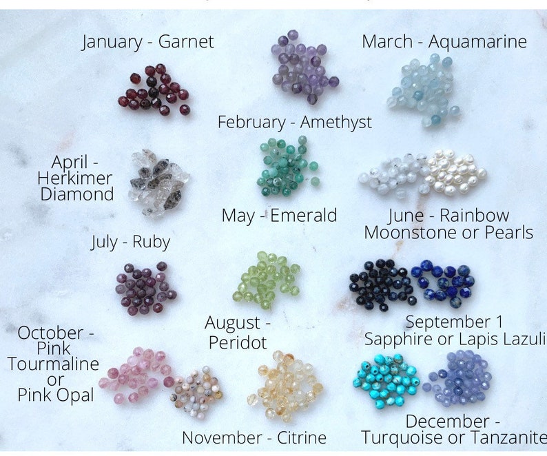 May include: A chart showing birthstones for each month of the year. The chart features a collection of small, colorful gemstones arranged in rows. Each row is labeled with the month and the corresponding birthstone. For example, January is Garnet, February is Amethyst, March is Aquamarine, April is Herkimer Diamond, May is Emerald, June is Rainbow Moonstone or Pearls, July is Ruby, August is Peridot, September is Sapphire or Lapis Lazuli, October is Pink Tourmaline or Pink Opal, November is Citrine, and December is Turquoise or Tanzanite.