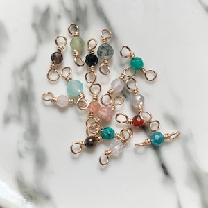 May include: Assortment of gemstone beads with gold-toned wire loops. The beads are in various colors, including green, blue, red, brown, and white.
