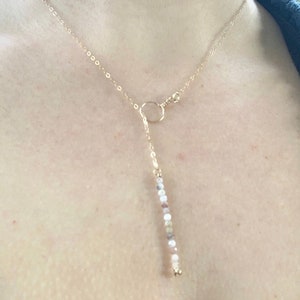May include: A gold chain necklace with a circle pendant and a long, beaded drop. The beads are a mix of white, pink, and gold.