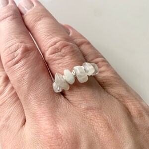 Könnte beinhalten: Ein Ring aus Silberdraht mit weißen Mondstein-Chips. Der Ring befindet sich an einem Finger.