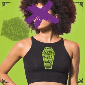 May include: A black crop top featuring a graphic of a coffin ticket that reads "General Admission One Welcome to Hell No Refunds". The background is a bright green colour.