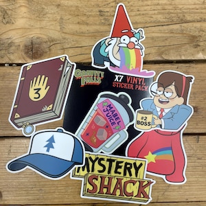 May include: A selection of vibrant vinyl stickers featuring characters and imagery from the animated series Gravity Falls. Includes a gnome, a book, a hat, and the words "Mystery Shack" and "Mabel Juice".