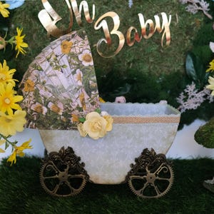 May include: A white baby carriage with a floral patterned canopy and gold accents. The carriage is decorated with a yellow flower and a gold ribbon. The carriage is sitting on a green grassy surface.