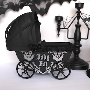 May include: A black gothic-themed baby carriage. The carriage has a bat-shaped hood, decorative wheels, and the words "Baby Bat" in a stylized font. Black roses and lace trim enhance the spooky design. A candelabra is visible in the background.