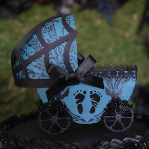May include: A decorative baby carriage in teal and black. The carriage features a black bow, intricate cutouts, and decorative wheels. The teal body has a pattern and baby footprints. The carriage is a unique item.