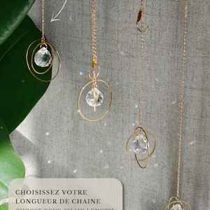 May include: Four gold-toned metal chain ornaments with clear faceted crystal pendants suspended within gold rings. The text reads: CHOISISSEZ VOTRE LONGUEUR DE CHAINE, CHOOSE YOUR CHAIN LENGTH, 5 CM | 2 IN: COMPACT, 20 CM | 8 IN: VERSATILE, 50 CM | 20 IN: LONG.