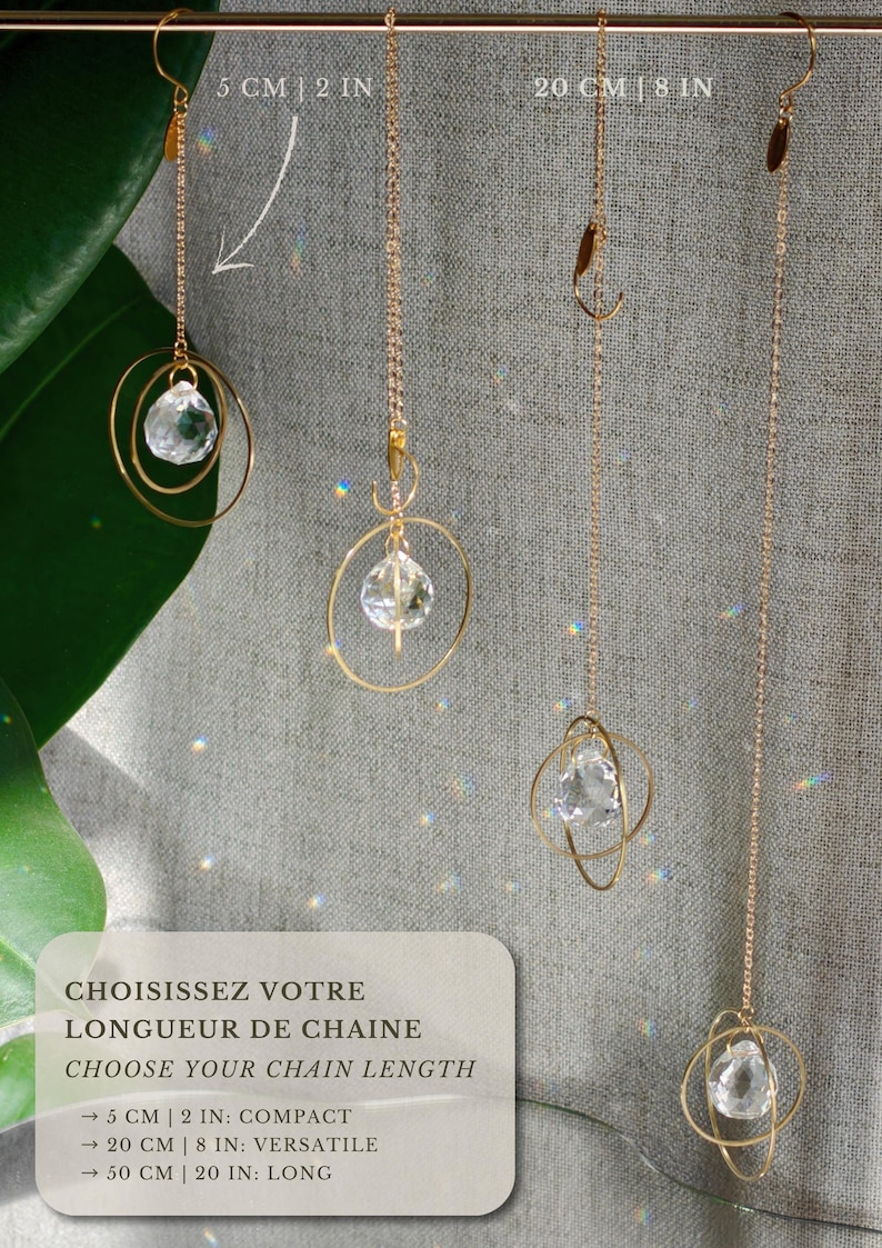May include: Four gold-toned metal chain ornaments with clear faceted crystal pendants suspended within gold rings. The text reads: CHOISISSEZ VOTRE LONGUEUR DE CHAINE, CHOOSE YOUR CHAIN LENGTH, 5 CM | 2 IN: COMPACT, 20 CM | 8 IN: VERSATILE, 50 CM | 20 IN: LONG.