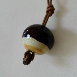 May include: A brown leather cord necklace with a round, dark brown and cream ceramic pendant.