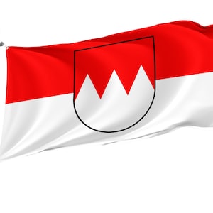 Puede incluir: Una bandera roja y blanca con un escudo negro y blanco que presenta tres picos blancos. La bandera ondea al viento.