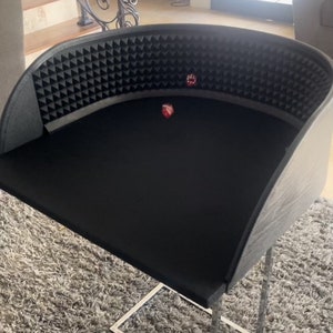 May include: A black tabletop gaming surface with a curved, padded back and a silver metal stand. Two red dice are on the surface.