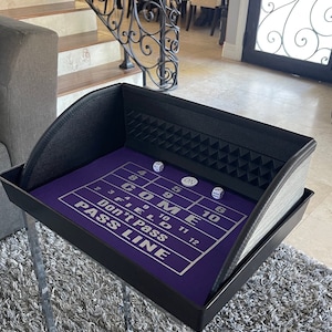May include: A purple felt craps table with a black leather frame and dice on the felt. The table has the numbers 2 through 12 printed on it, along with the words "Come", "Don't Pass", "Pass Line", and "Field".