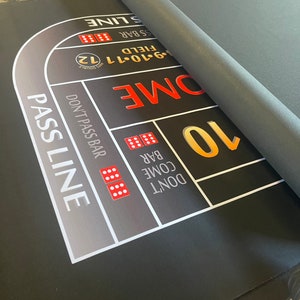 May include: A black felt craps table with white and gold markings. The table has a pass line, don't pass bar, come bar, don't come bar, and field areas. The table also has a 10, 9-10-11, 12, and a 'Don't Pass Bar' area.