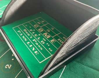 Puede incluir: Una bandeja de plástico negro con un inserto de fieltro verde. El fieltro tiene líneas blancas y las palabras "COME", "FIELD", "DON'T PASS" y "PASS LINE" impresas en él. La bandeja tiene una tapa de plástico negro curvada.