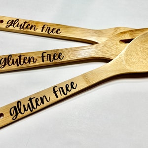 Peut inclure: Trois cuill&egrave;res en bois avec les mots "sans gluten" grav&eacute;s sur les manches. Les cuill&egrave;res sont en bambou naturel et ont une couleur brun clair.