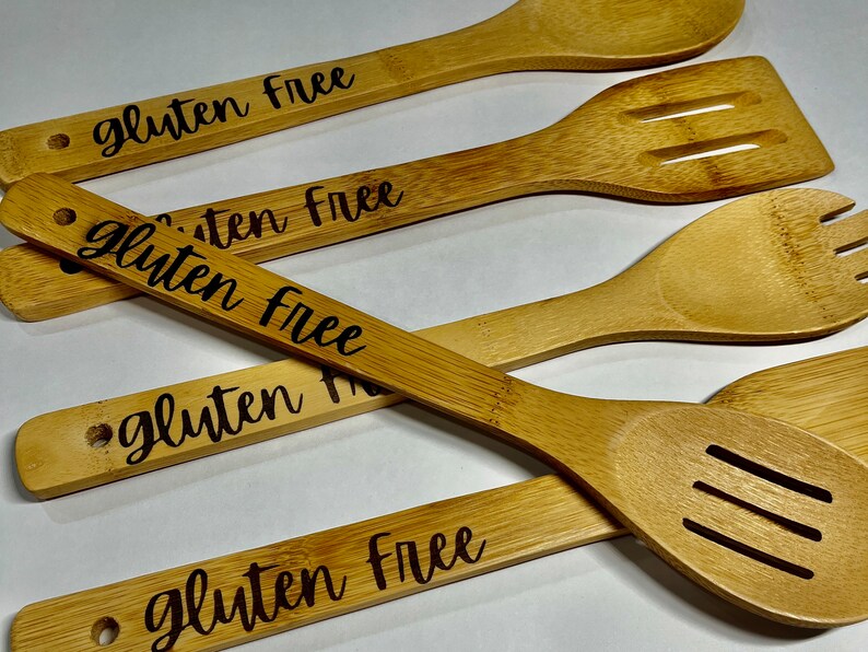 Peut inclure: Ensemble de quatre cuill&egrave;res en bois avec les mots "sans gluten" grav&eacute;s sur chacune. Les cuill&egrave;res sont en bambou naturel et ont une couleur brun clair.