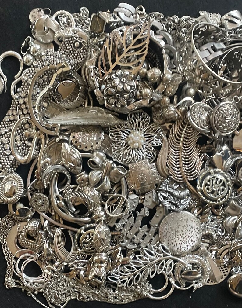 Puede incluir: Un mont&oacute;n grande de joyas plateadas, incluyendo collares, pulseras, pendientes, anillos y broches. Las joyas est&aacute;n dispuestas en un patr&oacute;n aleatorio, y algunas piezas se superponen.