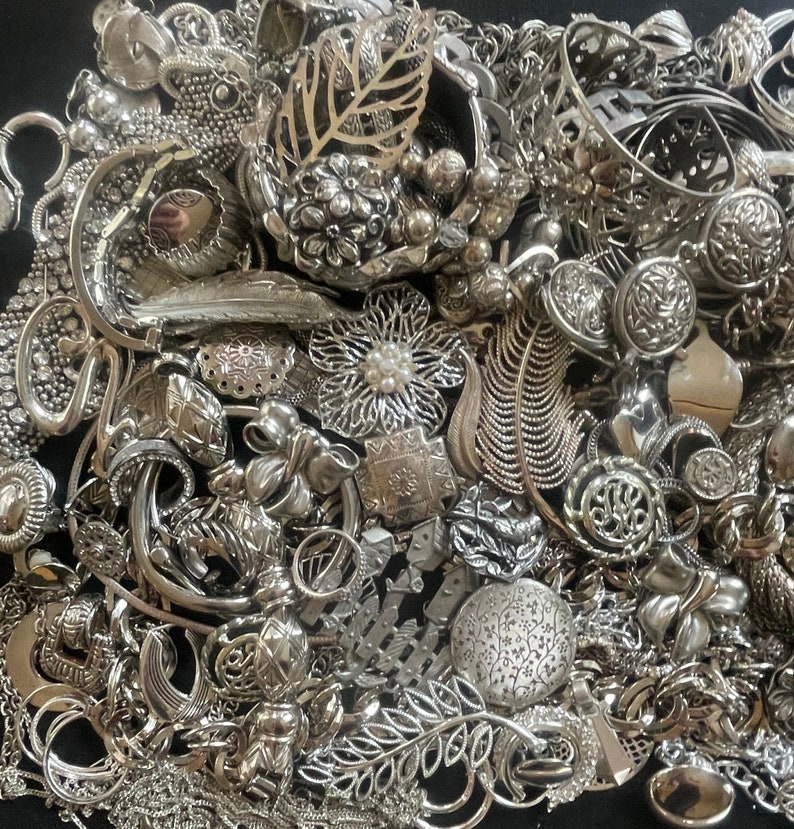 Puede incluir: Un mont&oacute;n grande de joyas plateadas, incluyendo collares, pulseras, pendientes y broches. Las joyas est&aacute;n dispuestas en un patr&oacute;n aleatorio, y algunas piezas se superponen. Las joyas est&aacute;n hechas de metal y tienen una variedad de dise&ntilde;os.