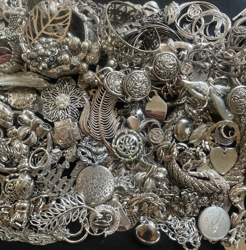 Puede incluir: Una gran colecci&oacute;n de abalorios de joyer&iacute;a plateados, que incluyen dise&ntilde;os florales, hojas y formas abstractas. Los abalorios est&aacute;n dispuestos en un patr&oacute;n aleatorio y parecen estar hechos de metal.