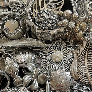 Puede incluir: Una colecci&oacute;n de piezas de joyer&iacute;a plateadas, que incluyen pulseras, collares, broches y pendientes. La joyer&iacute;a est&aacute; dispuesta en una pila, y algunas de las piezas se superponen. La joyer&iacute;a est&aacute; hecha de metal y tiene una variedad de dise&ntilde;os.