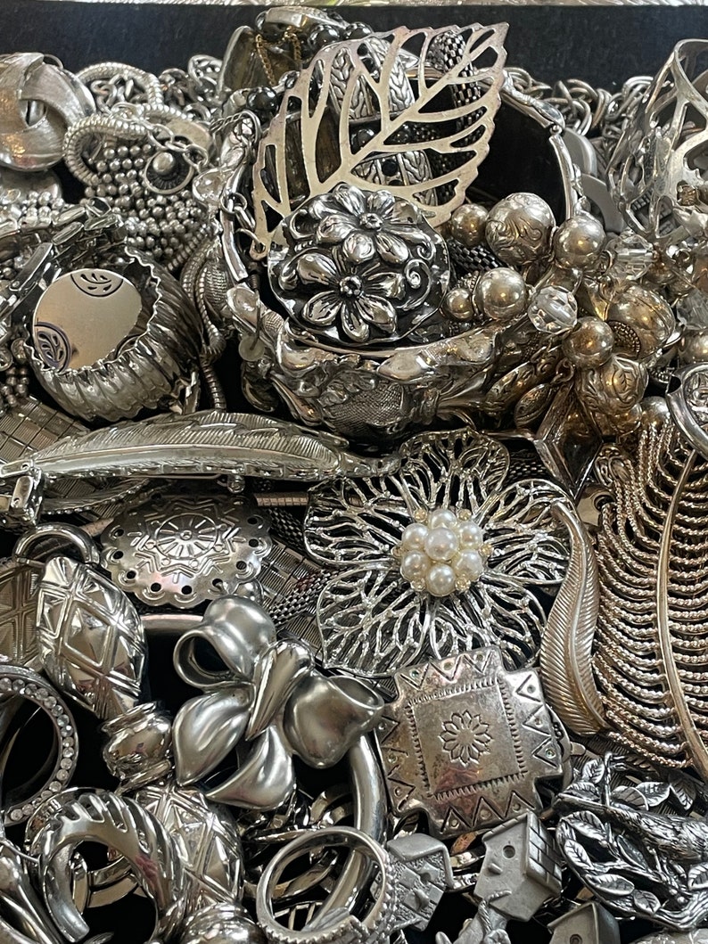 Puede incluir: Una colecci&oacute;n de piezas de joyer&iacute;a plateadas, que incluyen pulseras, collares, broches y pendientes. La joyer&iacute;a est&aacute; dispuesta en una pila, y algunas de las piezas se superponen. La joyer&iacute;a est&aacute; hecha de metal y tiene una variedad de dise&ntilde;os.