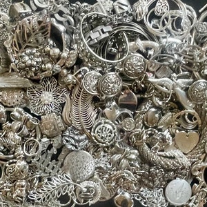 Puede incluir: Una gran colecci&oacute;n de abalorios de joyer&iacute;a plateados, incluyendo colgantes, cuentas y botones. Los abalorios est&aacute;n dispuestos en un patr&oacute;n aleatorio y todos tienen diferentes formas y tama&ntilde;os.