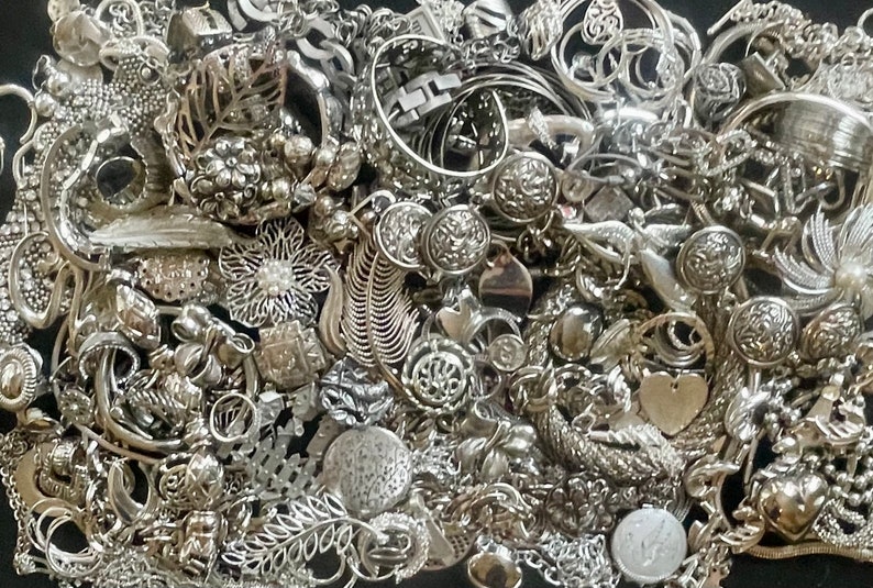 Puede incluir: Una gran colecci&oacute;n de abalorios de joyer&iacute;a plateados, incluyendo colgantes, cuentas y botones. Los abalorios est&aacute;n dispuestos en un patr&oacute;n aleatorio y todos tienen diferentes formas y tama&ntilde;os.