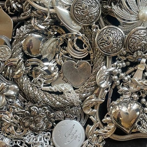 Puede incluir: Una colecci&oacute;n de joyas plateadas con diferentes formas y dise&ntilde;os, incluyendo corazones, flores y patrones geom&eacute;tricos. Las joyas est&aacute;n hechas de metal y tienen un acabado brillante.